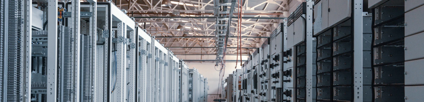 A long aisle between rows of rack-mounted equipment under a steel roof truss.