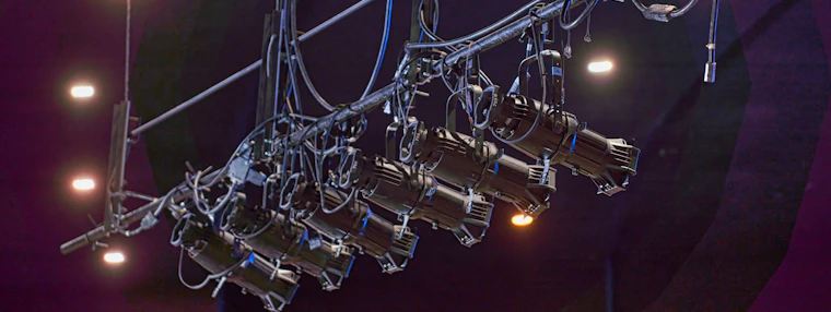 A row of theatre lanterns rigged on an overhead lighting bar.